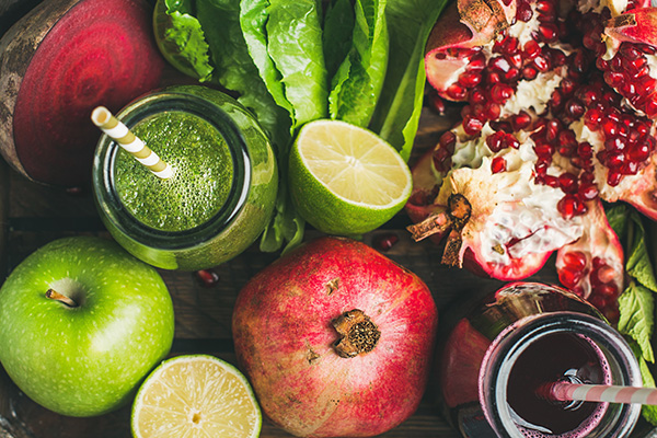 Green and purple fresh juices or smoothies with fruit, greens, vegetables in wooden tray, top view, selective focus